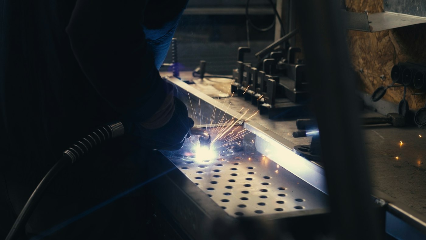 A welder working on a steel frame with sparks flying