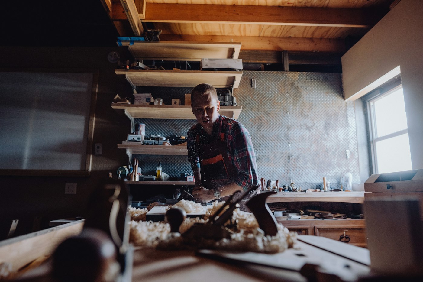 A woodworker shaping timber at a bench in a timber-beamed workshop